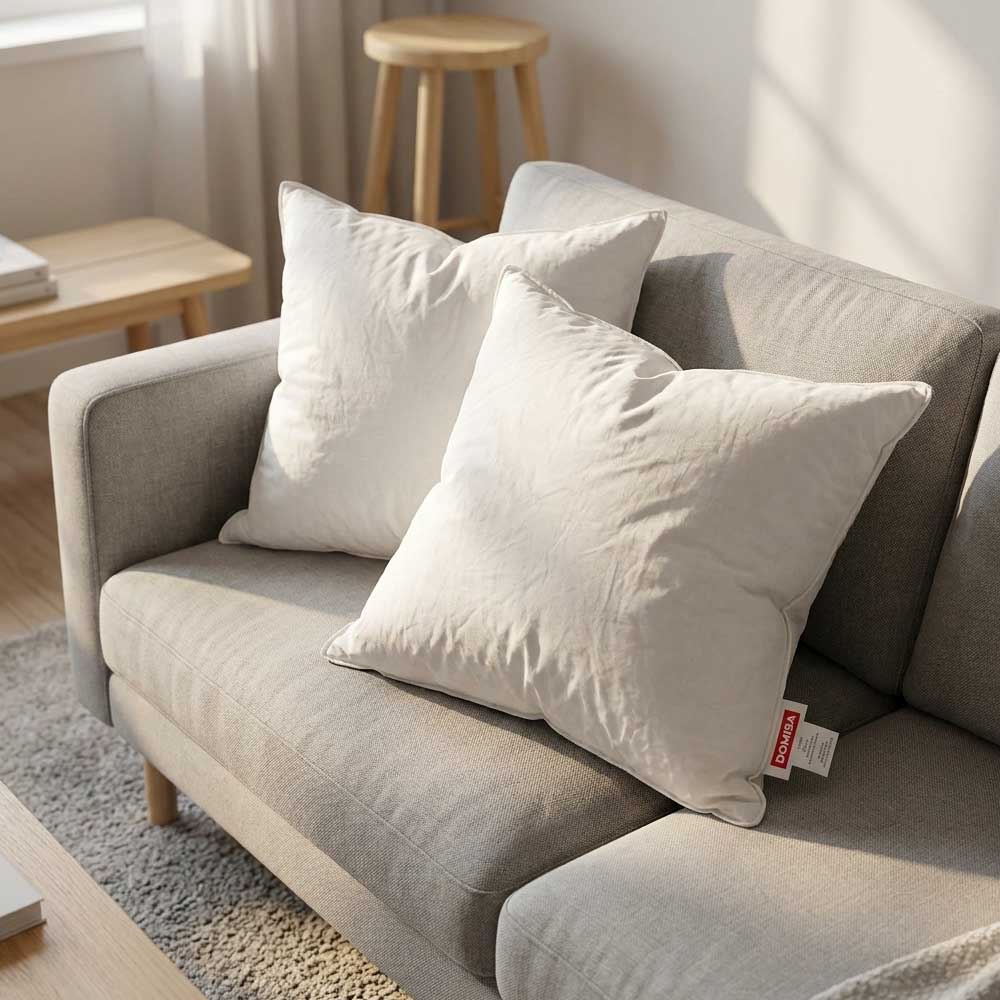 Set doua perne Ovia 40x40 cm albe, din pene de gasca asezate pe canapea