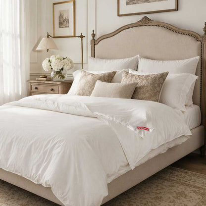 Set de pat Domisa Serene compus din două perne albe de 50x70 cm și o pilotă albă de 200x220 cm, umplute cu 90% puf și 10% pene de gâscă naturală, prezentate pe un pat elegant cu lenjerie albă imaculată